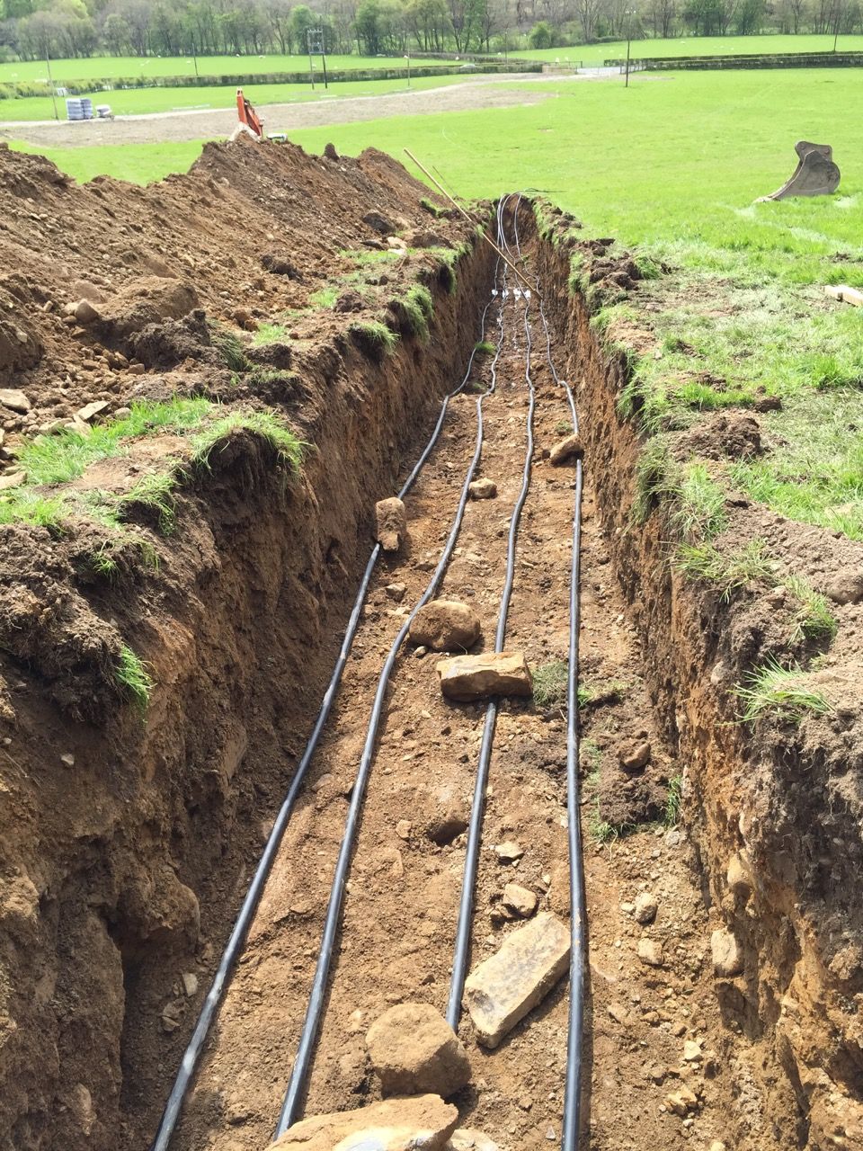 Long trench across a field with ground-loop pipes laid in it