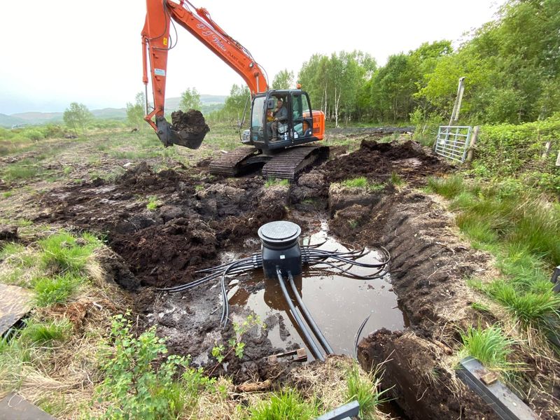 Digger excavating a pit for the ground-loop pipework, with the loop pipes emerging from the ground