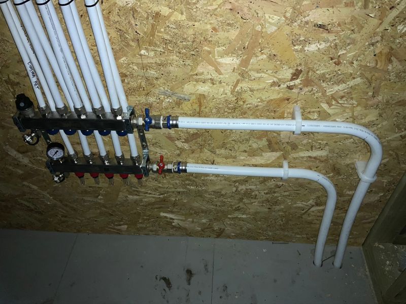 Heating manifold with valves mounted on an OSB wall, pipes rising to the ceiling